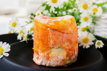 Soft cheese Langre. French soft cheese with white mold and orange rind Langre on a black matte plate. The cheese from Russian farms is made according to a French recipe. Close-up