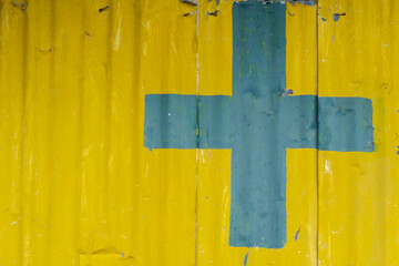 A cross on a yellow metal wall background alerts you to safety when approaching a building area. Cross symbol on a yellow background and Copy Space for entering text.
