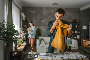 Adult man iron the wardrobe on the iron board while woman clean dust