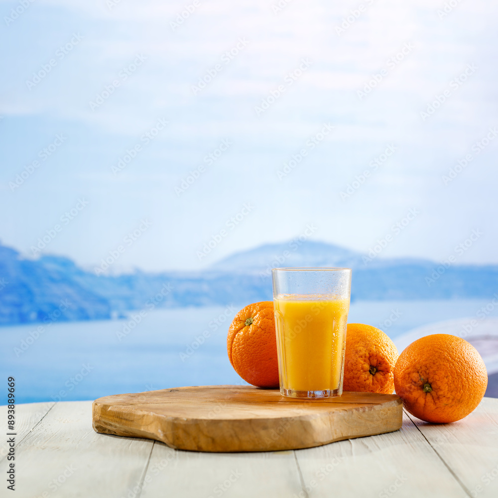 Wall mural Orange fruit and orange juice on white wooden board table with seascape with blue sky background. Copy space for products.