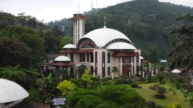 erial view of a beautiful white mosque with a tall minaret located in a lush green hillside area. Bogor - indonesia