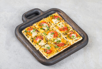 Mini square pies with tomatoes, ham, mozzarella, pesto, sesame seeds. On a plate	. Light gray background