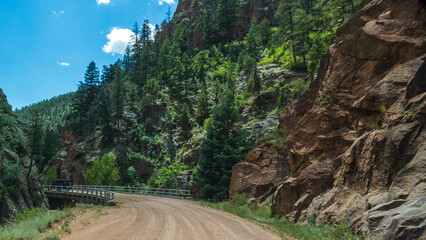 Curve  and bridge on historic Phantom Canyon Road in the mountains of Colorado; steep granite embankments covered in trees; concepts of scenic gold belt byway, adventure, and road less traveled