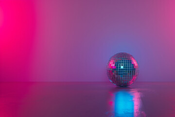 A sparkling disco ball sits on a glossy surface under vibrant pink and blue spotlights, reflecting colorful lights around a minimalist room.