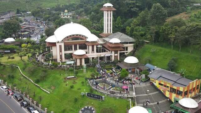 erial view of a beautiful white mosque with a tall minaret located in a lush green hillside area. Bogor - indonesia