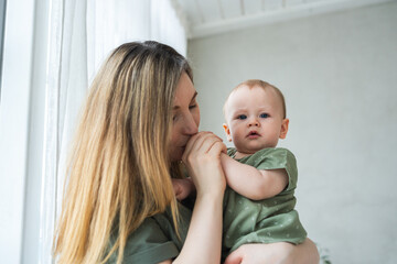 Happy family at home. Mother holding little toddler child daughter. Mom and baby girl relax playing having fun together at home. Mother hugging kissing baby with love care. Mom of breast feeding baby