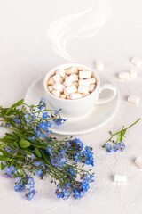 White Cup of hot cocoa with marshmallows And forget-me-nots flowers on a white background, Good morning postcard, Copy space