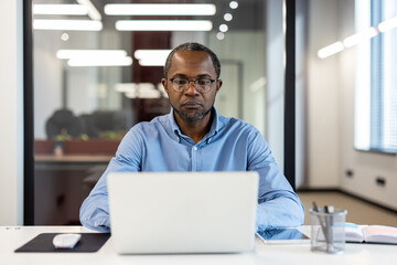 Businessman working on laptop in modern office. Professional setting promoting concentration and productivity. Well-lit room with contemporary design elements enhancing work environment.