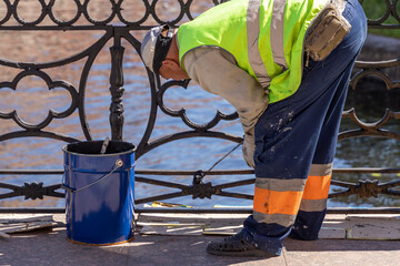 A man in a safety vest is painting a railing