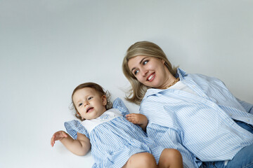 Happy family concept. Beautiful young mother lying on floor with her cute little 1 year old girl, looking at camera isolated at studio over white background