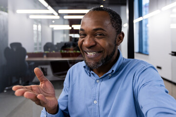 Confident businessman smiling and gesturing during video call in modern office setting. Professional communication, positive interaction, and friendly atmosphere captured in contemporary workspace