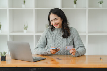 Happy and attractive Asian woman using smartphone and laptop holding credit card, shopping online during vacation