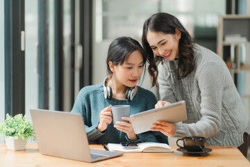 Two beautiful Asian businesswomen working together with tablets in the office