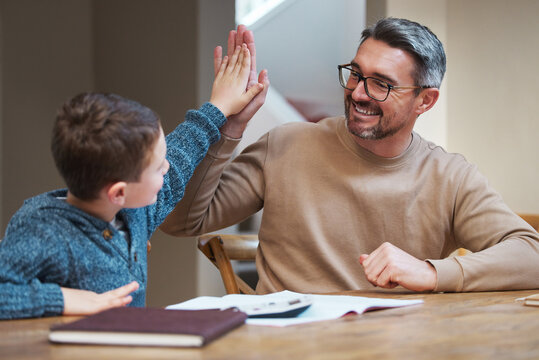 Homework, dad and child at table with high five for support, learning and winning at school project. Celebration, achievement and father studying in home with son for help, advice and education goals