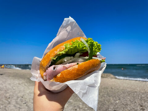 Traditional north germany snack street food Fischbroetchen matjes fish fillet with onion and salad leaves in a wheat bun in female hand close up on Baltic sea beach 