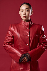 Fashion asian brunette woman in red leather jacket posing confidently with hands on hips for camera
