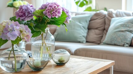 Hortensia bouquet and glass bowls on wooden coffee table with cozy sofa and pillows. Living room...