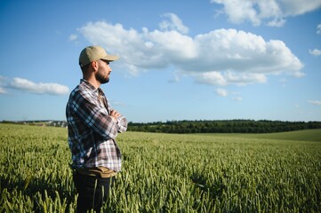 Happy bearded farmer in cap standing on agricultural wheat field