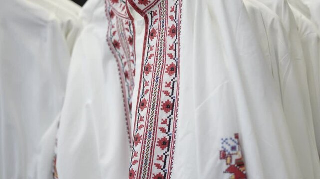 Close-up view of traditional Bulgarian embroidered shirts, showcasing intricate red and black patterns, displayed in a shop setting. Perfect representation of Bulgarian cultural attire.