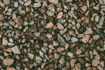 Top view of many crushed granite stones of small size and different shapes of a reddish hue, evenly poured and laid. The lower stones have a damp surface due to recent rain.
