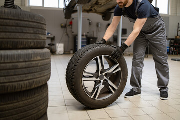 Mechanic changing car tire in professional auto repair shop. Worker in uniform handling tire for maintenance and repair. Automotive service concept captured in garage environment.