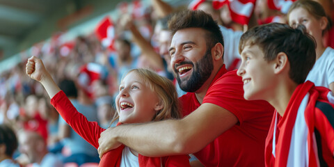 Fototapeta premium Excited sports fans wearing red and white clothes celebrating the victory of their team. People chanting and cheering for their soccer team. Family watching football match.
