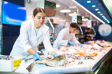 Portrait of saleswoman offering fresh fish atlantic cod at seafood shop