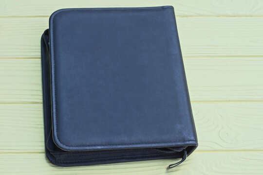 one big closed black notepad with leather cover lies on a yellow wooden table