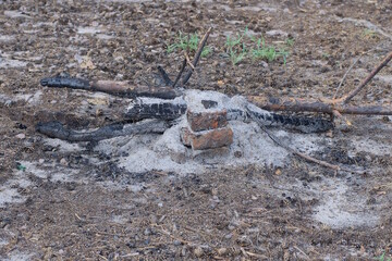 an extinct fire made of black ash and ash and brown branches and bricks on the  ground on the street