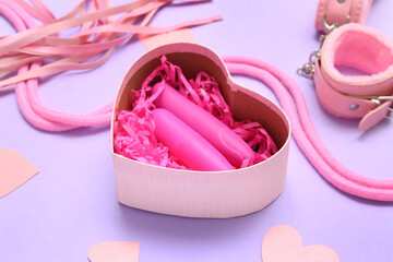 Gift box with sex toys and paper hearts on lilac background, closeup