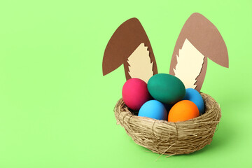 Nest with bunny ears and Easter eggs on green background