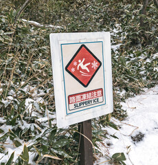A sign with a picture of a person slipping and the Japanese hieroglyphs for slippery ice. Red...