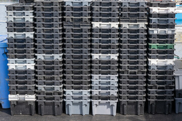 Black, grey, and white colored empty plastic fish crates or bins stacked on a wharf. Multiple rows...