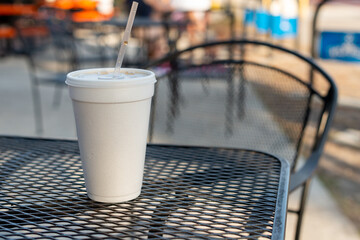 A large or tall white non recyclable to-go drink cup with a plastic lid and straw on a black metal...