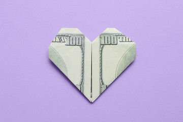 Origami heart made of dollar banknotes on lilac background