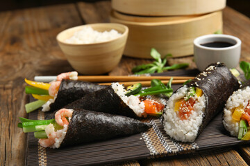 Bamboo mat with tasty sushi cones, rolls, soy sauce and boiled rice on wooden background, closeup