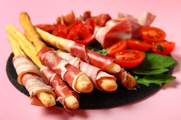 Slate plate of tasty Italian Grissini with bacon on pink background, closeup