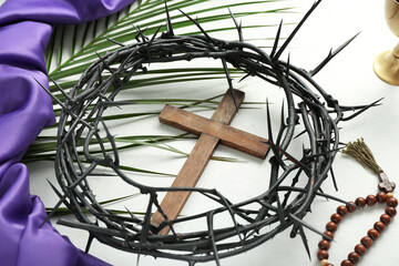 Wooden cross with crown of thorns and palm leaf on white background, closeup. Good Friday concept