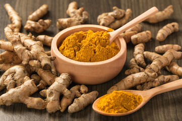 Turmeric powder in wooden bowl with turmeric root on wooden table .