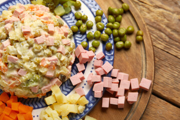 Plate of tasty Olivier salad and ingredients on wooden background, closeup