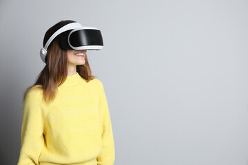Smiling woman using virtual reality headset on light grey background. Space for text