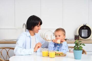Young mother with her little son having breakfast at table in kitchen