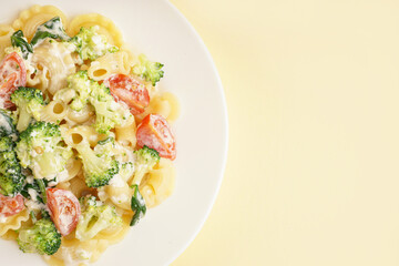 Plate of tasty pasta with broccoli and tomatoes on yellow background