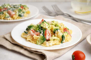 Plate of tasty pasta with broccoli, tomatoes and napkin on white background