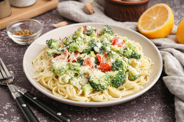 Plate of tasty pasta with broccoli and tomatoes on grunge grey background