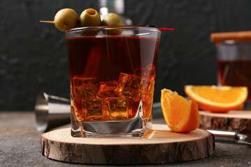 Wooden board with glass of Old Fashioned Cocktail, olives and orange slice on grey grunge table