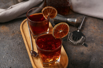 Wooden tray with glasses of Old Fashioned Cocktail, dried orange slices and spoon on grey grunge background