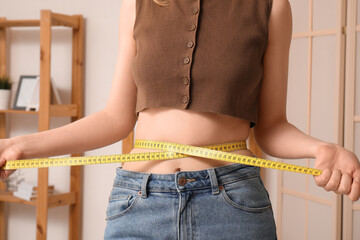 Young woman measuring her waist at home. Weight loss concept