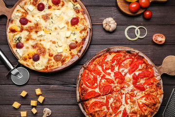 Boards with tasty pizzas, tomatoes, garlic and cutter on wooden background