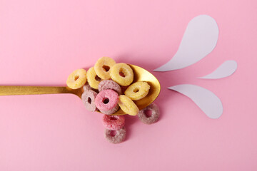 Spoon with colorful sweet cereal rings and paper milk drops on pink background